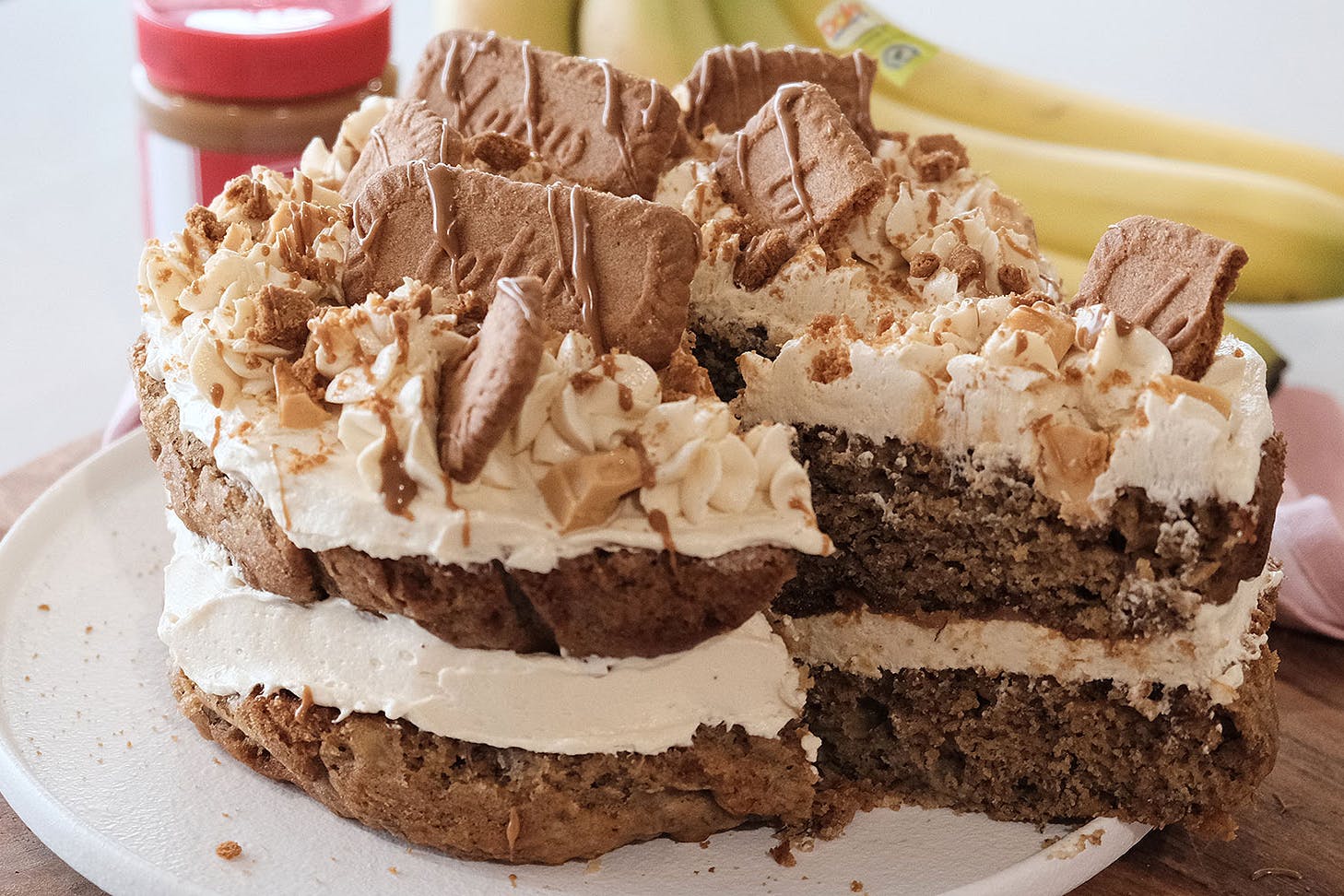 A two-tier banana Biscoff cake layered with cream cheese icing and topped with Biscoff cookies, white chocolate chunks, and Biscoff drizzle.